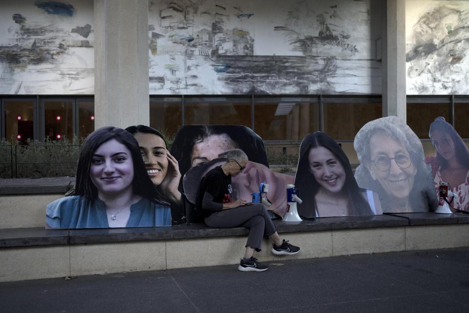 An activist sits with large photos depicting women held hostage by Hamas in the Gaza Strip before a march by families and their supporters to call on Israeli Prime Minister Benjamin Netanyahu's government to make a deal to free their loved ones, in Tel Aviv, Israel, Wednesday, May 8, 2024. (AP Photo/Maya Alleruzzo)