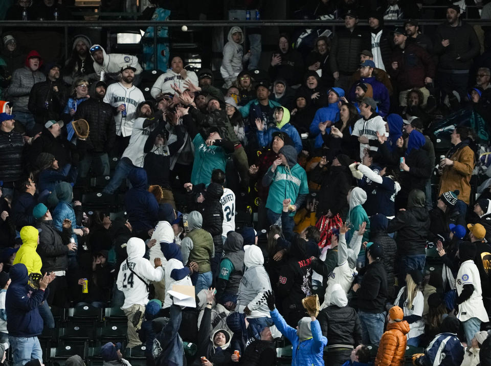 Fans vie for a solo home run hit by Cleveland Guardians' Andres Gimenez off Seattle Mariners relief pitcher Diego Castillo in the seventh inning during a baseball game Saturday, April 1, 2023, in Seattle. (AP Photo/Lindsey Wasson)