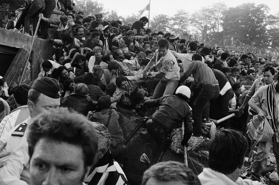 FILE - In this May 29, 1985 file photo, a crowd of soccer fans try to escape a collapsed wall prior to the start of the European Cup final between Liverpool and Juventus, at the Heysel Stadium in Brussels. Liverpool had been the dominant team in the European Cup, winning four titles between 1977 and 1984. Friday, May 29, 2020 marks 35 years since 39 victims lost their lives during a European Cup football match between Liverpool and Juventus due to a surge of rival supporters resulting in a collapsed wall. (AP Photo/Gianni Foggia, File)