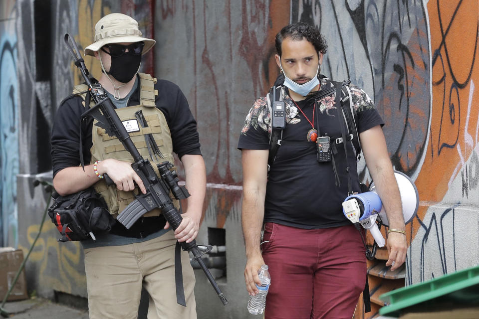 A person who said he goes by the name James Madison, left, carries a rifle as he walks with Javi Cordero, Saturday, June 20, 2020, inside what has been named the Capitol Hill Occupied Protest zone in Seattle. Both men are part of the volunteer security team who have been working inside the CHOP zone. A pre-dawn shooting Saturday near the area left one person dead and critically injured another person, authorities said Saturday. The area has been occupied by protesters after Seattle Police pulled back from several blocks of the city's Capitol Hill neighborhood near the Police Department's East Precinct building. (AP Photo/Ted S. Warren)