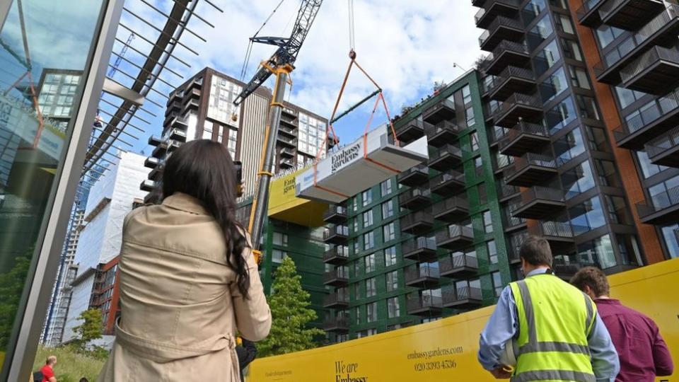 Gente viendo como una grúa levanta una piscina de acrílico transparente que se colocará entre dos bloques de apartamentos en Embassy Gardens, junto a la nueva Embajada de EE.UU. en el suroeste de Londres, el 28 de septiembre de 2020.