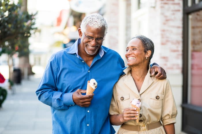 Smiling couple eating ice cream and walking down a sidewalk.