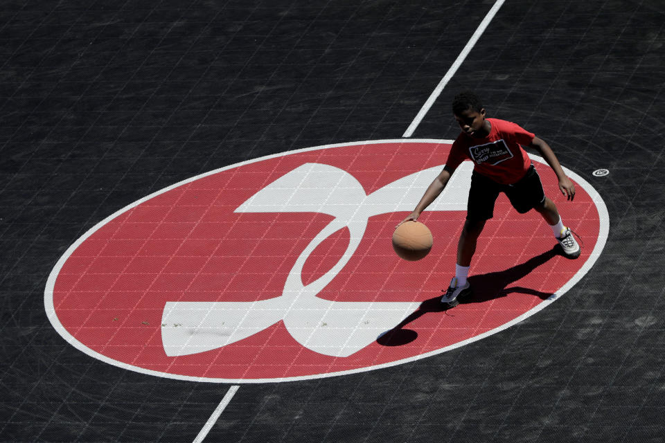 FILE - In this July 1, 2019, file photo the logo for Under Armour, which is based in Baltimore, is seen at half court as Neko Coleman, 10, plays basketball during a summer day at Federal Hill Park in Baltimore. Under Armour last week said it would up to $425 million in restructuring charges as it tries to reverse a decline in sales in ’s latest warning about sales and costs put another dent in its stock price and added to a years-long decline. (AP Photo/Julio Cortez, File)