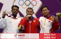 Cuba's Leuris Pupo (C) bites his gold medal he won in the 25m rapid fire pistol men's final at the London 2012 Olympic Games as he stands on the podium with silver medalist India's Vijay Kumar (L) and bronze medalist China's Ding Feng at the Royal Artillery Barracks in London, on August 3, 2012. AFP PHOTO/MARWAN NAAMANI