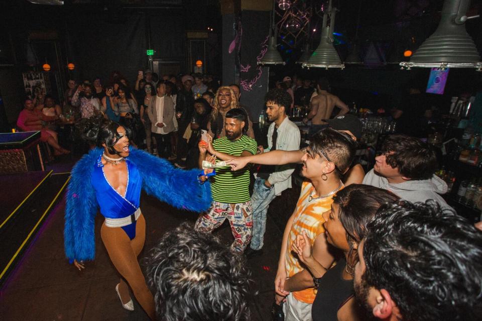 A drag performance in a blue long-sleeved bodysuit walks among the crowd at a show.