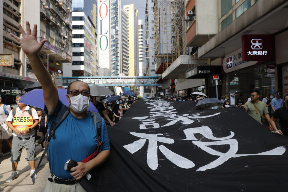A protester wears a mask and holds up his hand to represent the five demands as he walks with a protest slogan banner in Hong Kong on Saturday, Oct. 5, 2019. All subway and trains services are closed in Hong Kong after another night of rampaging violence that a new ban on face masks failed to quell. (AP Photo/Vincent Thian)