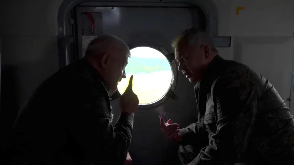 Russian Defense Minister Sergei Shoigu and Colonel General Yevgeny Nikiforov sit closely together against what appears to be the interior door of an aircraft.