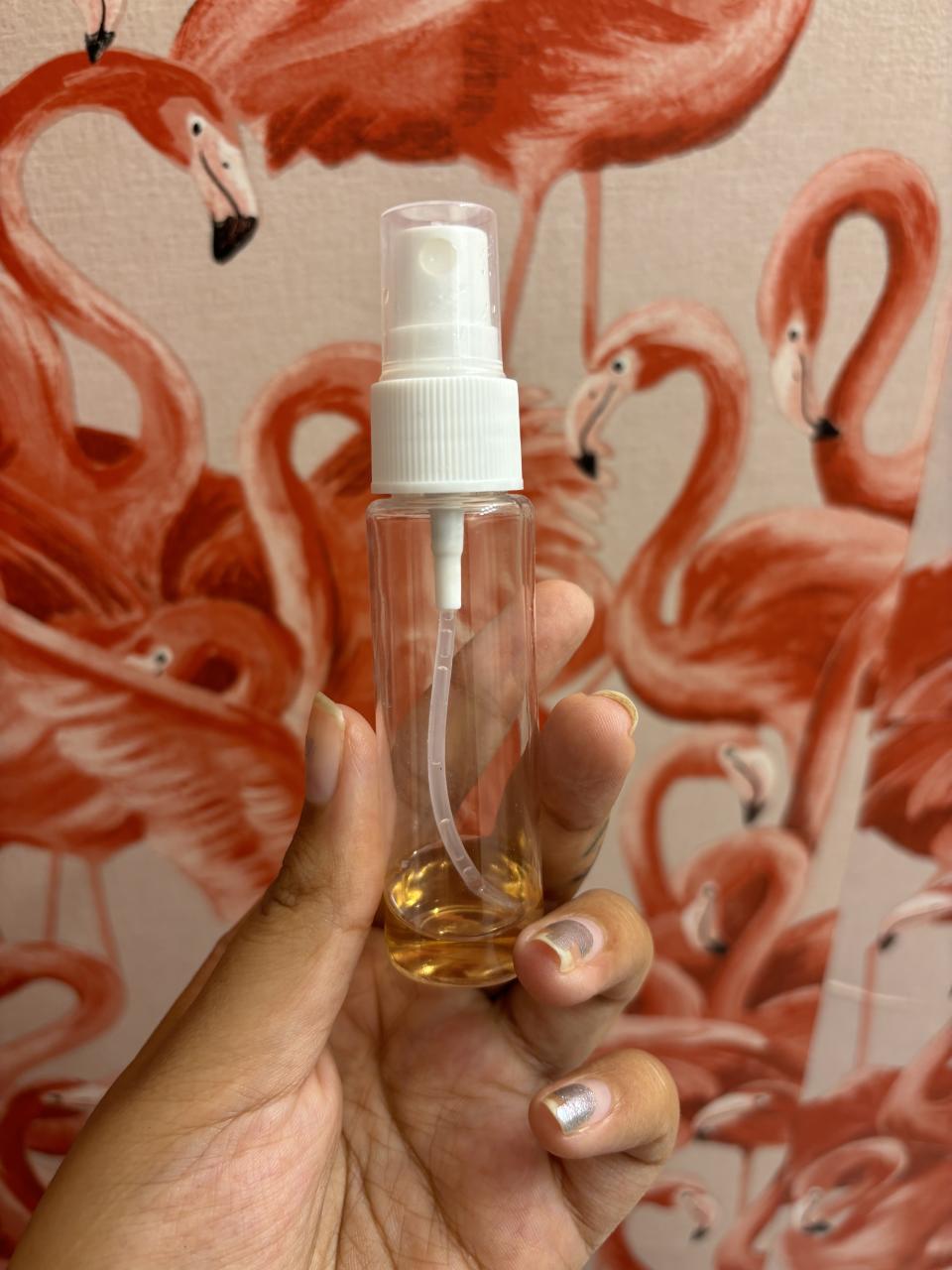 Hand holding glycolic acid in clear spray bottle in front of flamingo wallpaper