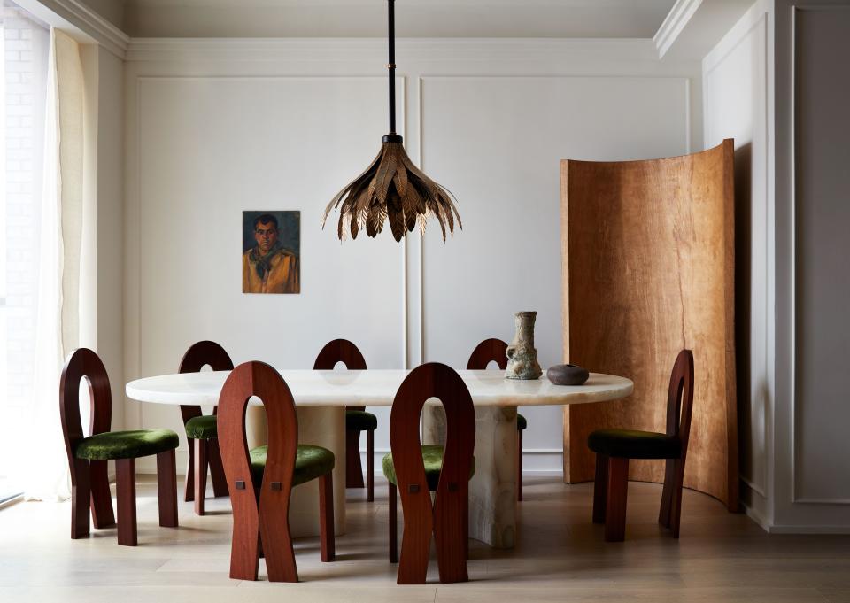 The dining room features a white-onyx dining table that was custom-made in Italy; its oval shape is echoed in the solid wooden screen behind it, an oak piece from Oliver Gustav. Above the table is an oxidized-brass pendant by Dimore Studio. “It’s the only bit of flair in the room,” says Valle of the fixture’s feather-like shapes. The chairs were designed by Valle.