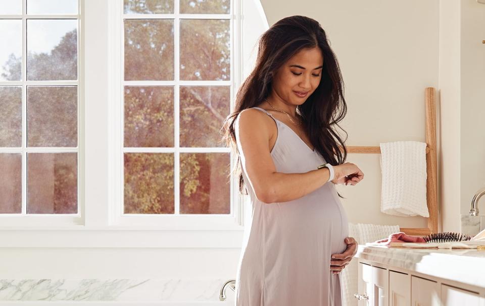 a pregnant woman looking at her white fitbit