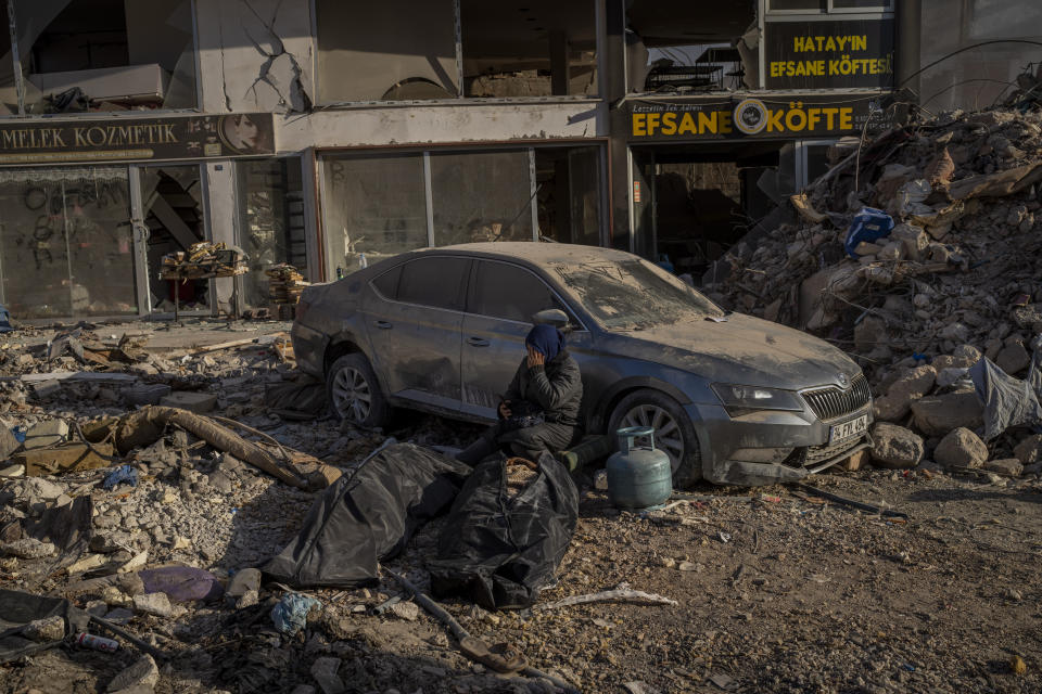 A woman sits next to bodies that were pulled from the rubble of a destroyed building in Antakya, southeastern Turkey, Wednesday, Feb. 15, 2023. The earthquakes that killed more than 39,000 people in southern Turkey and northern Syria is producing more grieving and suffering along with extraordinary rescues and appeals for aid. (AP Photo/Bernat Armangue)