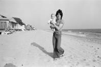 <p>Ronnie Wood of the Rolling Stones carries his baby Jesse James Wood on the beach of their Malibu home in 1977.</p>