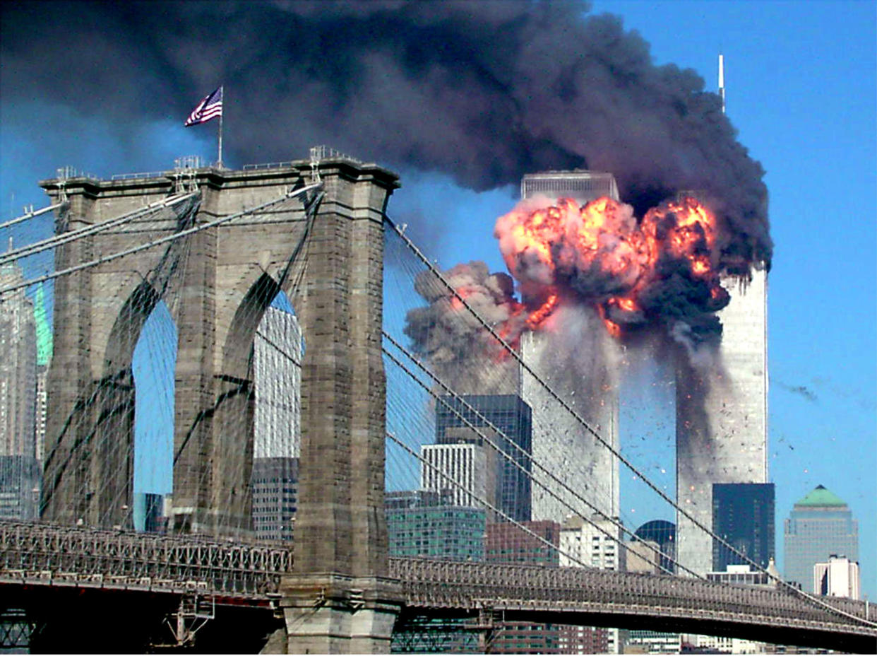 The top floors of one of the World Trade Center towers explodes into flames, with the Brooklyn bridge in the foreground.
