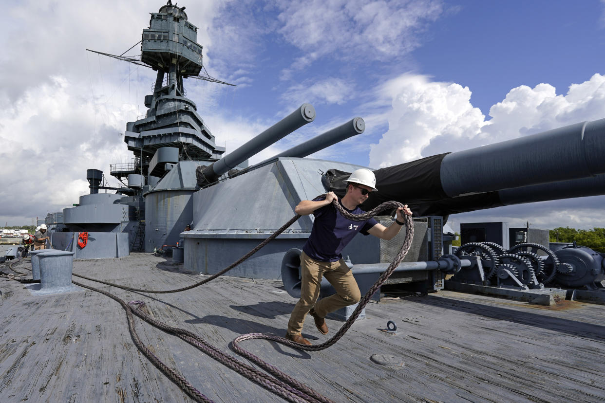 Hunter Miertschin helps secure a rope on the USS Texas Tuesday, Aug. 30, 2022, in La Porte, Texas. The vessel, which was commissioned in 1914 and served in both World War I and World War II, is scheduled to be towed down the Houston Ship Channel Wednesday to a dry dock in Galveston where it will undergo an extensive $35 million repair. (AP Photo/David J. Phillip)