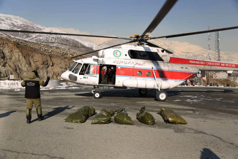 In this photo released by Iran's Red Crescent Society, bags containing bodies of mountaineers who died after avalanches in a mountainous area north of the capital are placed on the ground carried by a rescue helicopter, Iran, Saturday, Dec. 26, 2020. A series of avalanches in Iran killed multiple people on Friday following strong winds and snowfall a day earlier. (Iran's Red Crescent Society via AP)