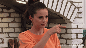 Selena Gomez on her cooking show making a gesture for "call me" in her kitchen