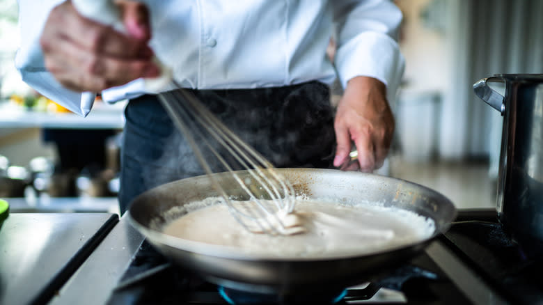 chef using French whisk in pan on stove