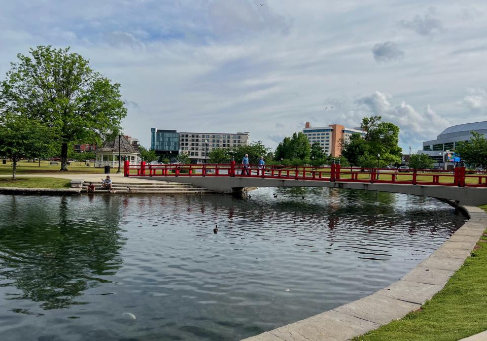 big spring park in huntsville alabama, water and red bridge with trees to the left and a building in the background