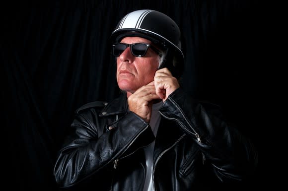 Man in leather jacket and sunglasses strapping on a helmet