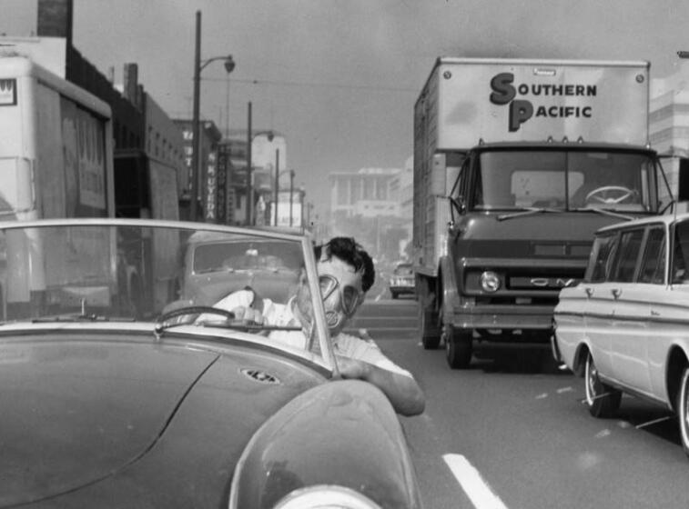 Los Angeles, California-1966- In the smog battle a Los Angeles commuter wears an only slightly satiric gas mask on October 2, 1966. Automotive experts show how a new smog device cuts down on the emission of car fumes, while testifying before the California Assembly. ( Los Angeles Herald Examiner Photo Collection/Los Angeles Public Library)