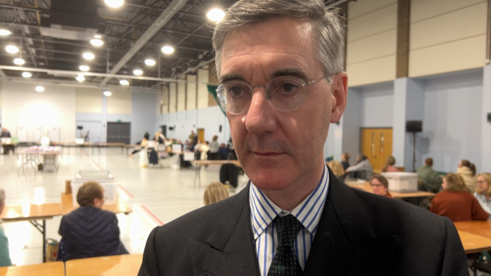 Jacob Rees-Mogg looking past a camera lens, wearing a stripy shirt and dotted tie.