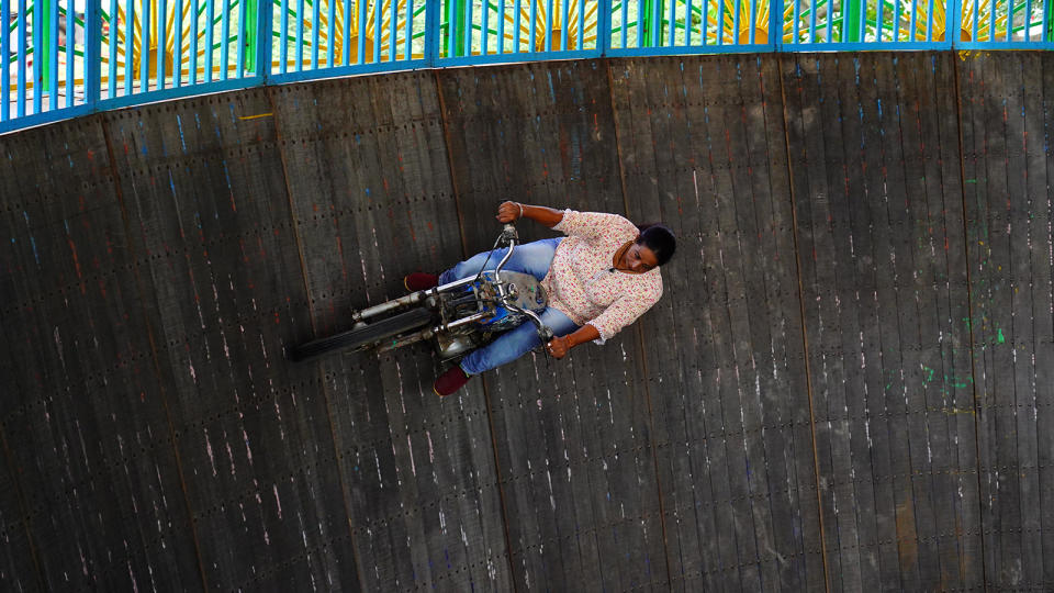 A woman rides a motorcycle in the "Well of Death." She is vertical to the ground, using centrifugal force to stay on the wall.