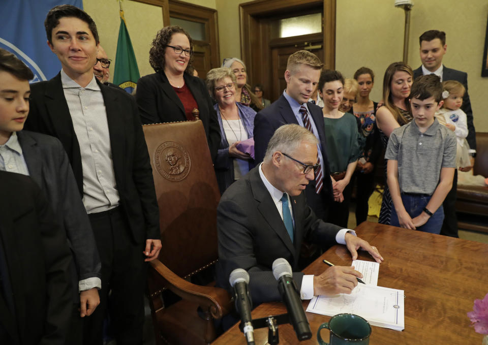 Katrina Spade, upper left, the founder and CEO of Recompose, a company that hopes to use composting as an alternative to burying or cremating human remains, looks on Tuesday, May 21, 2019, as Washington Gov. Jay Inslee, center, signs a bill into law at the Capitol in Olympia, Wash., that allows licensed facilities to offer "natural organic reduction," which turns a body, mixed with substances such as wood chips and straw, into soil in a span of several weeks. The law makes Washington the first state in the U.S. to approve composting as an alternative to burying or cremating human remains. (AP Photo/Ted S. Warren)