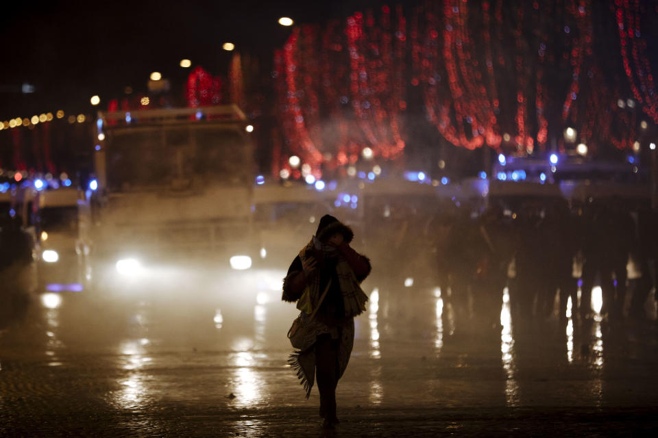 A demonstrator wearing a yellow vest walks as she stands amid tear gas on the Champs Elysees avenue in Paris, Saturday, Dec. 22, 2018. France's yellow vest protesters, who have brought chaos to Paris over the past few weeks with their economic demands, demonstrated in sharply reduced numbers Saturday at the start of the Christmas and New Year holidays. (AP Photo/Kamil Zihnioglu)