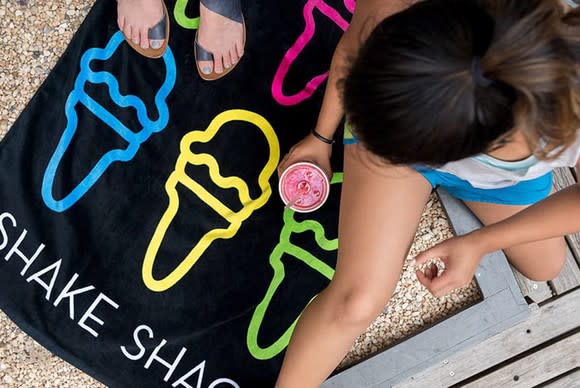 A girl sits on a Shake Shack towel.