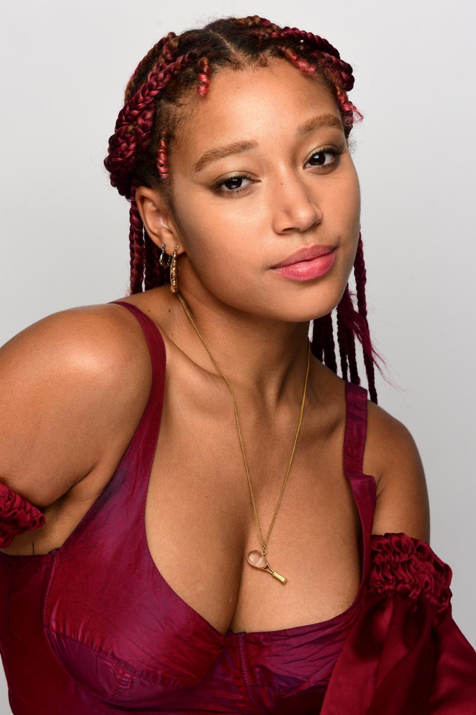 Amandla posing for a photo wearing a ruffled burgundy dress, with braided hair and a pendant necklace