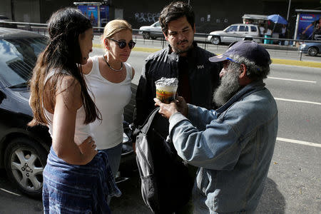 Diego Prada (2nd R) and Maria Luisa Pombo (2nd L), Volunteers of the Make The Difference (Haz La Diferencia) charity initiative, speak with a homeless man after giving him a cup of soup and an arepa in Caracas, Venezuela March 5, 2017. REUTERS/Marco Bello