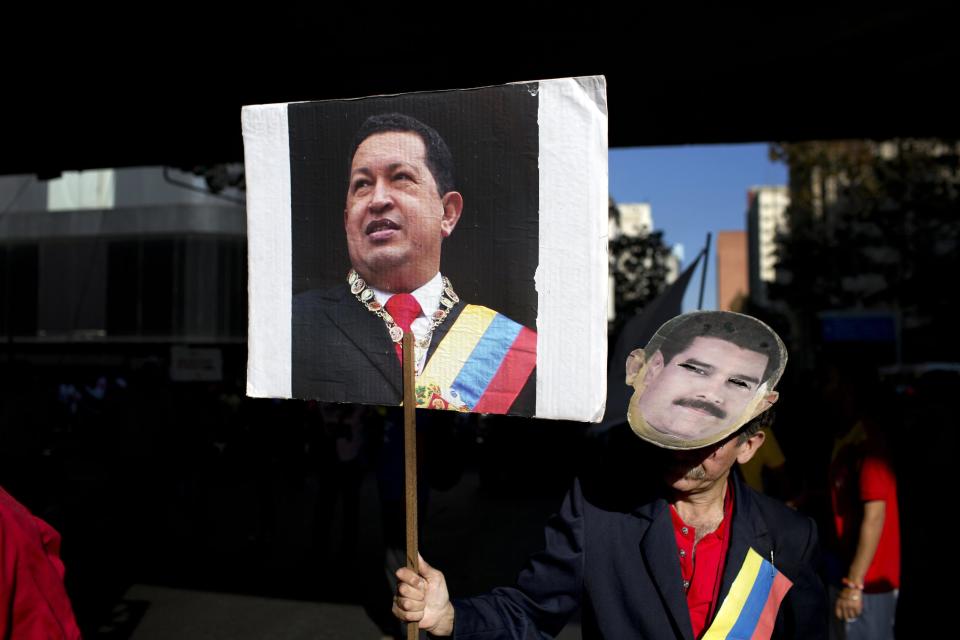 FILE.- In this Tuesday, Feb. 25, 2014 photo a worker from the National Telecommunications Company CANTV holds a sign of Venezuela's former President Hugo Chavez and wears a mask of current President Nicolas Maduro during a rally to show support for the government in Caracas, Venezuela. Heartfelt devotion is a crucial but fading force for Chavez’s hand-picked successor, President Nicolas Maduro. Despite daily invocations of his mentor, and control of the powerful party apparatus he inherited, Maduro is increasingly on his own in a fight against a destabilizing wave of anti-government protests.(AP Photo/Rodrigo Abd, File)