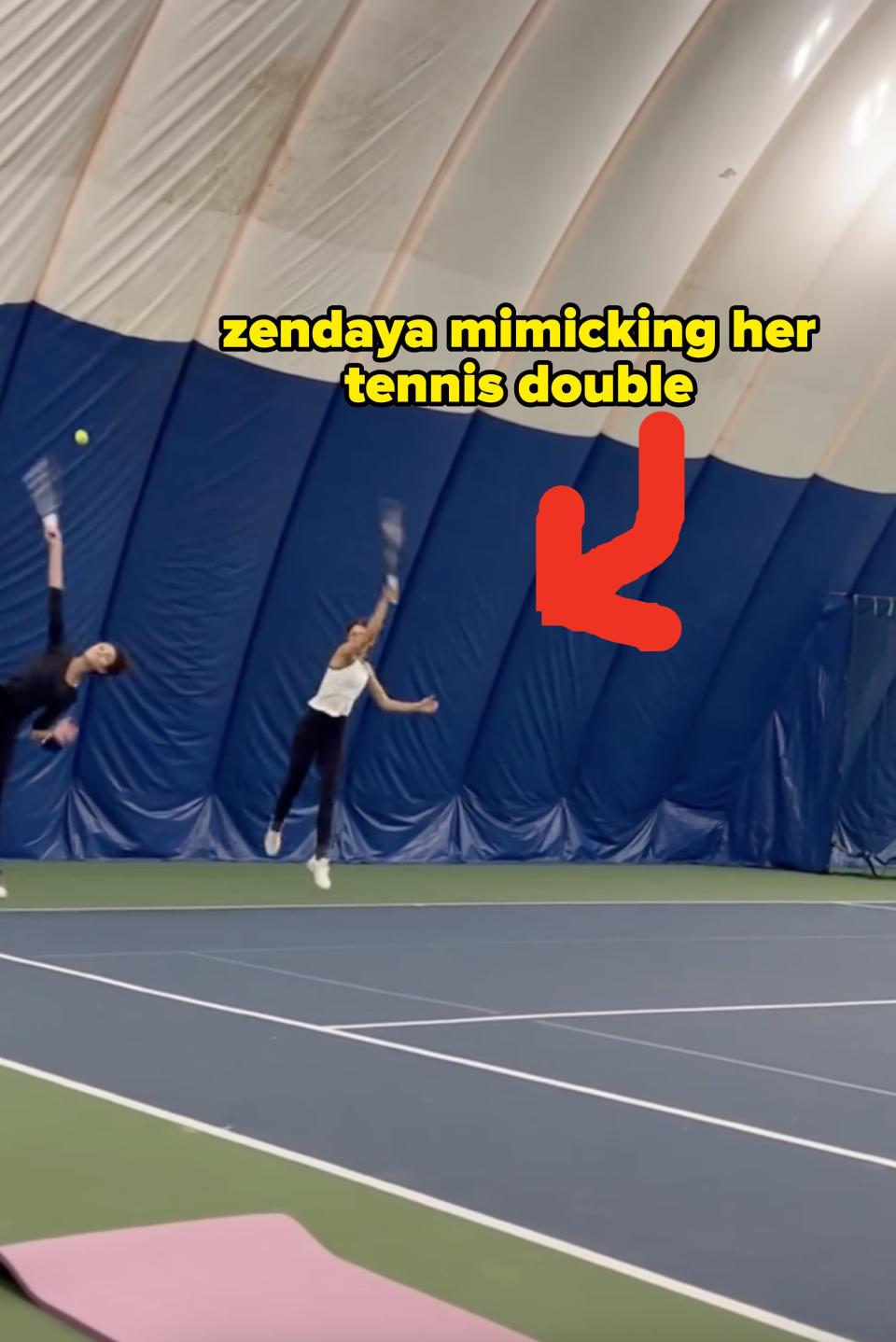 Two people playing tennis indoors, one reaching for an overhead shot