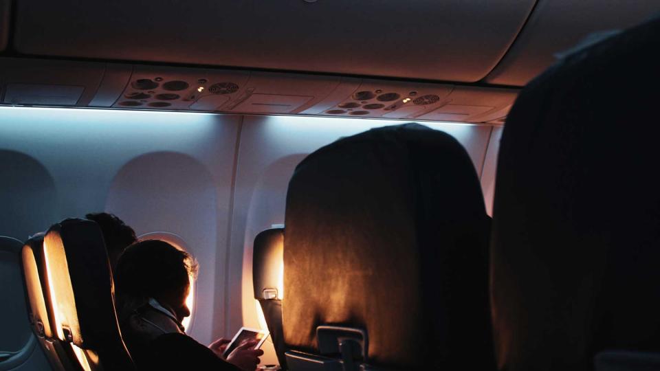 Passenger sleeping on a dimly lit airplane with the sun coming in through the windows