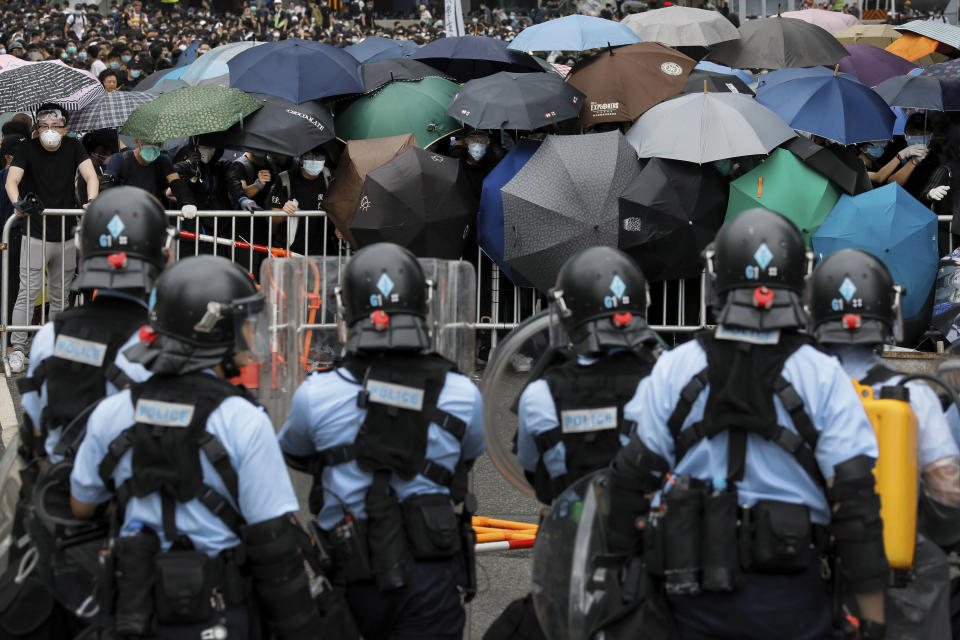 FILE - In this file photo taken Wednesday, June 12, 2019, policemen in riot gear stand watch as protesters use umbrellas to shield themselves near the Legislative Council in Hong Kong. Hong Kong's leader Carrie Lam is pushing forward amendments to extradition laws which would allow people to be sent to mainland China to face charges. The proposed legislation has triggered in recent days the largest protests in Hong Kong in more than a decade, as some residents fear this will be their last chance to speak out publicly without threat of arrest at mainland authorities' request.(AP Photo/Vincent Yu, File)