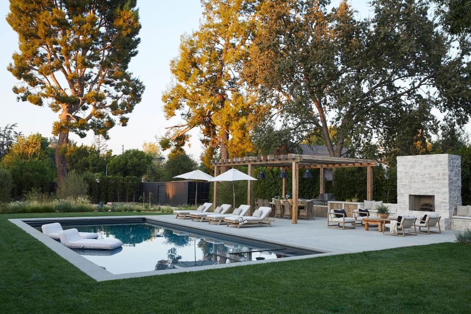 GSLA Studio designed the exterior landscaping to highlight the mature oak and olive trees on the property. During the remodel, Lewis added a pool with Fireclay Tile on the water line—with matching Oliver James floats—along with an outdoor fireplace coated in the same stone from the front of the home, seating area, and pergola built from vintage timber trucked to California from Ohio.