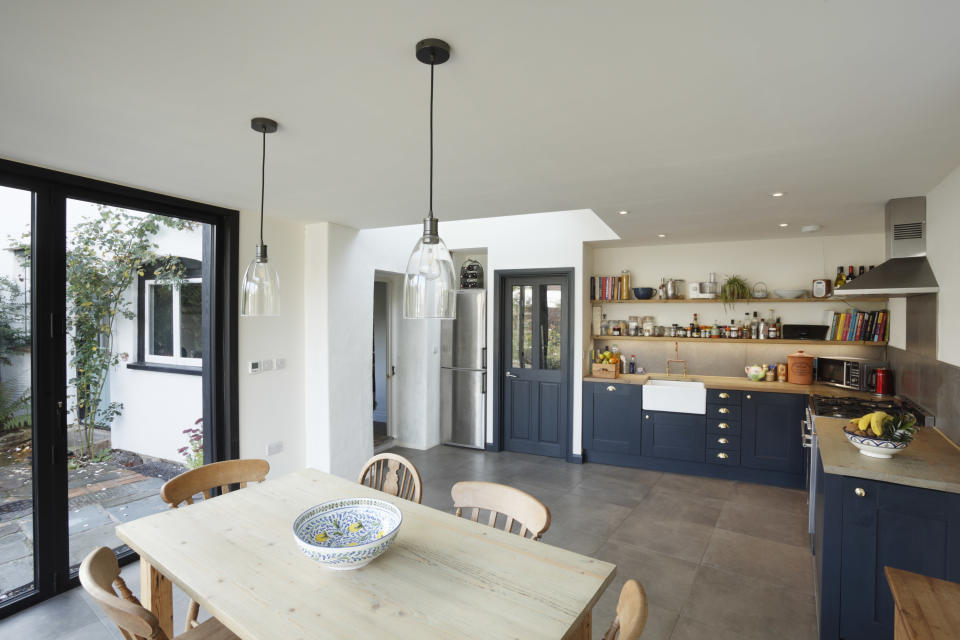 The interior of a kitchen with blue cabinets, big windows, and a wooden kitchen table