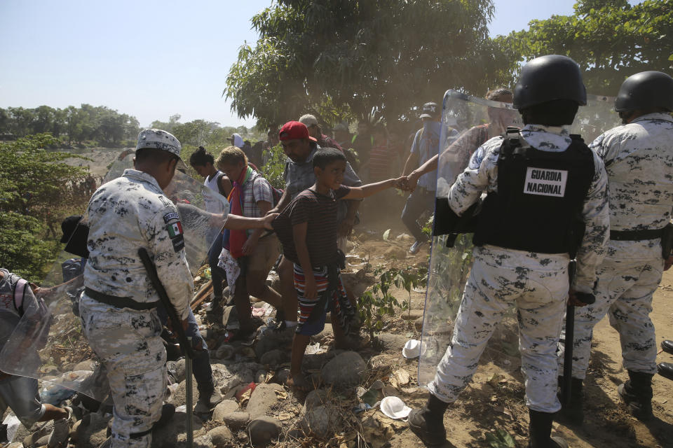 A young Central American migrant is held by fellow migrants as they are blocked by Mexican National Guards after they crossed the Suchiate River with a group of migrants from Guatemala to Mexico, on the riverbank near Ciudad Hidalgo, Mexico, Monday, Jan. 20, 2020. More than a thousand Central American migrants hoping to reach the United States marooned in Guatemala are walking en masse across a river leading to Mexico in an attempt to convince authorities there to allow them passage through the country. (AP Photo/Marco Ugarte)