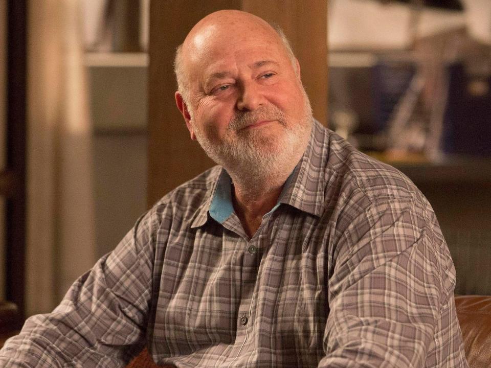 Rob Reiner as Bob sits on couch in a plaid gray shirt in loft