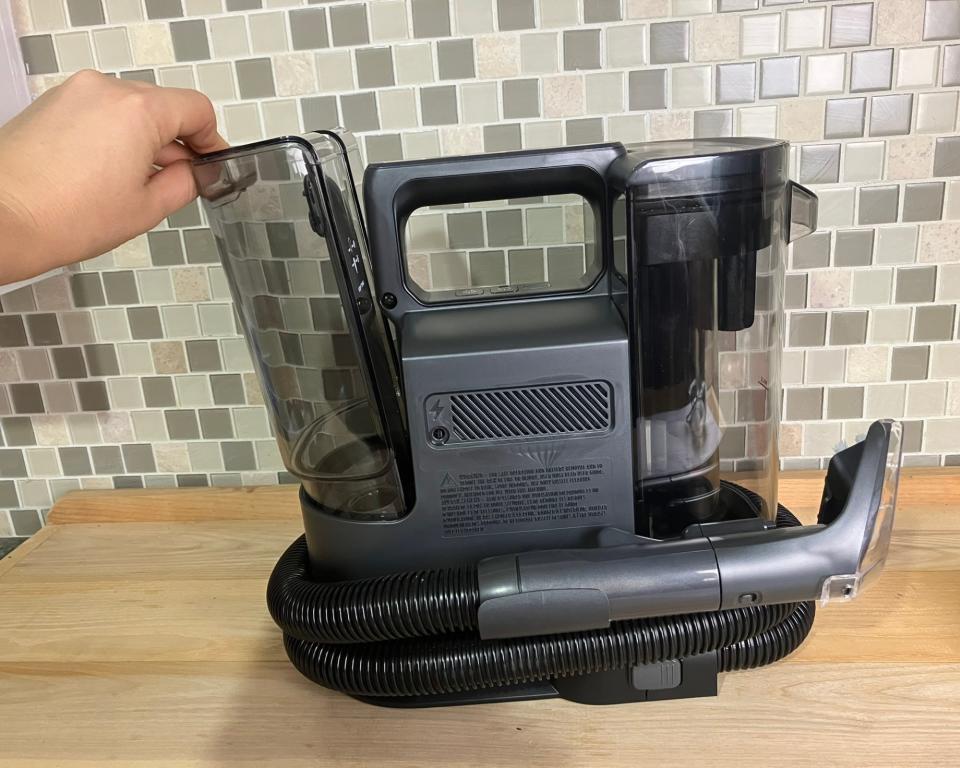 Paige Cerulli, a white woman removing the clean water tank from a Bissell Little Green Portable Carpet Cleaner on wooden kitchen worktop with green tiled kitchen wall