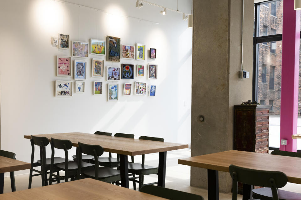 Four wooden desks with black chairs surrounding, a gallery wall with colorful artwork at Hope for Flowers.