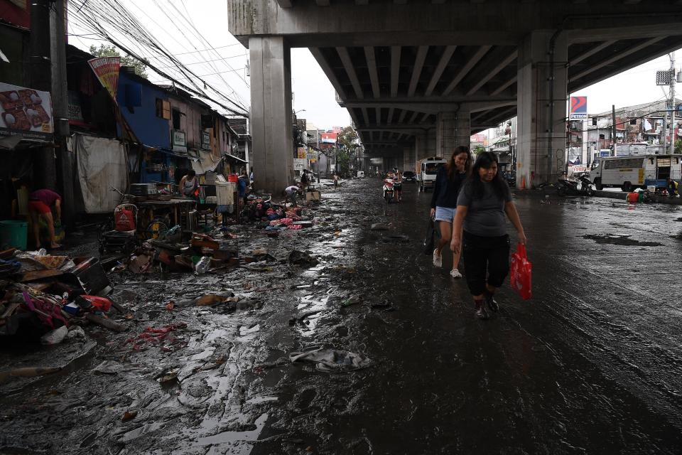 Residents walk along a mudded road caused by floodings in Manila (AFP via Getty Images)