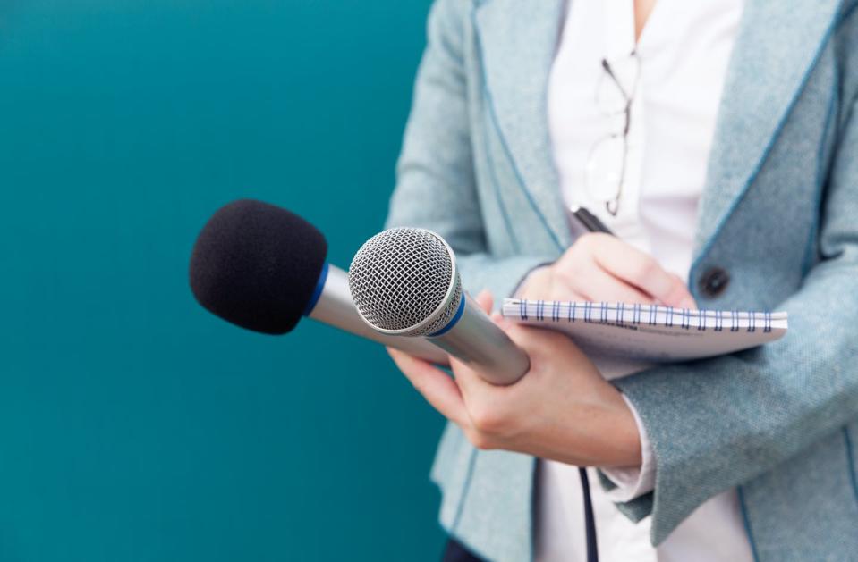 A woman holding two microphones and a reporter's pad.