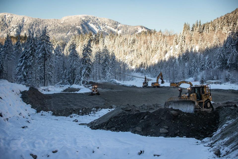 Heavy machinery moves dirt and debris near a snow covered forest.