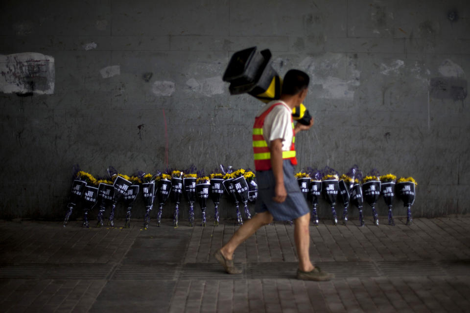 A roadworker walks past flowers placed under a bridge where a man drowned on Saturday, July 21 in his flooded car on a main road in Beijing Friday, July 27, 2012. Chinese characters on the wraps read "One Rain, One Day of Mourning." The storm that ravaged Beijing nearly a week ago and killed at least 77 people remains a sensitive topic in China, with a newspaper ordered to cut its coverage and online discussions curtailed. (AP Photo/Alexander F. Yuan)