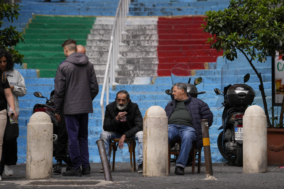 People sit in the street in front of stairs painted with the colors of the Italian flag and Napoli soccer team, in downtown Naples, Italy, Tuesday, April 18, 2023. It's a celebration more than 30 years in the making, and historically superstitious Napoli fans are already painting the city blue in anticipation of the team's first Italian league title since the days when Diego Maradona played for the club. (AP Photo/Andrew Medichini)