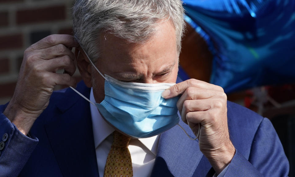 New York Mayor Bill de Blasio puts on a mask during a news conference outside the Mosaic Pre-K Center on the first day of school, Monday, Sept. 21, 2020, in New York. The city public schools delayed reopening for two weeks. (AP Photo/Mark Lennihan)