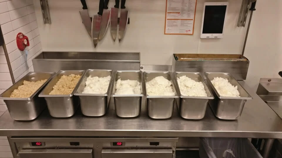 seven steel tubs filled with brown and white rice.