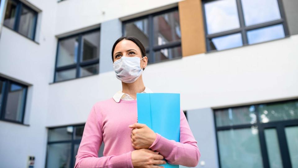 Low angle view of teacher with face mask after lockdown, walking outdoors in front of school.