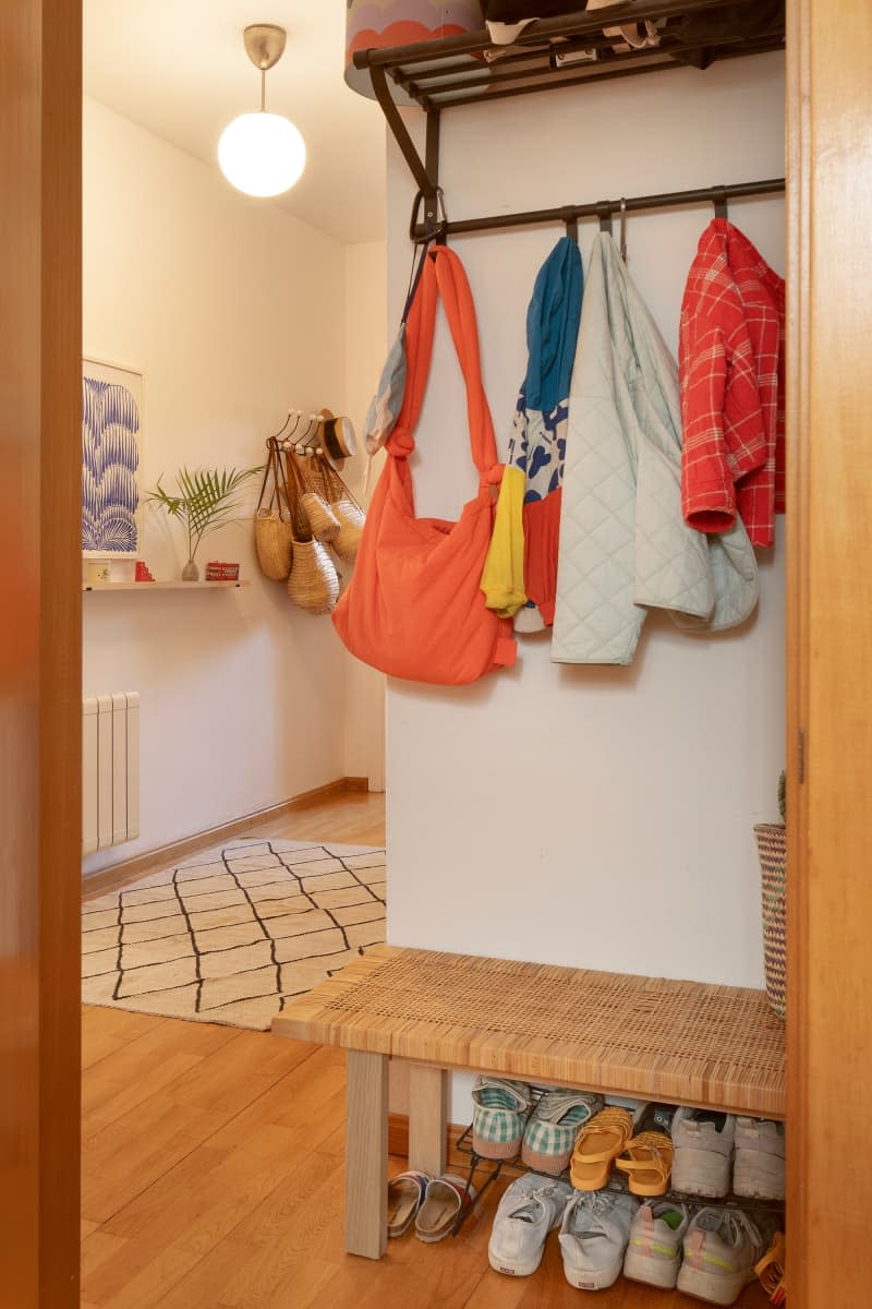 White entryway with hanging coats and bags and bench with shoe storage